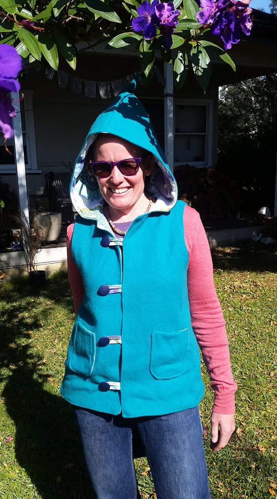 White woman wearing a Pippa Studios woollen vest standing in a sunny backyard, smiling.